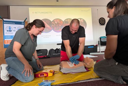 Zwei Mitarbeiter und der Sanitäter reanimieren die Übungspuppe